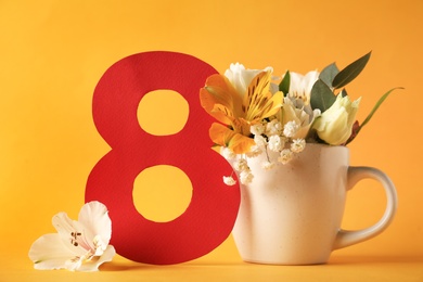 Photo of Beautiful flowers in cup and number 8 on yellow background. International Women's day