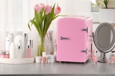 Photo of Pink mini cosmetics refrigerator and skin care products on table