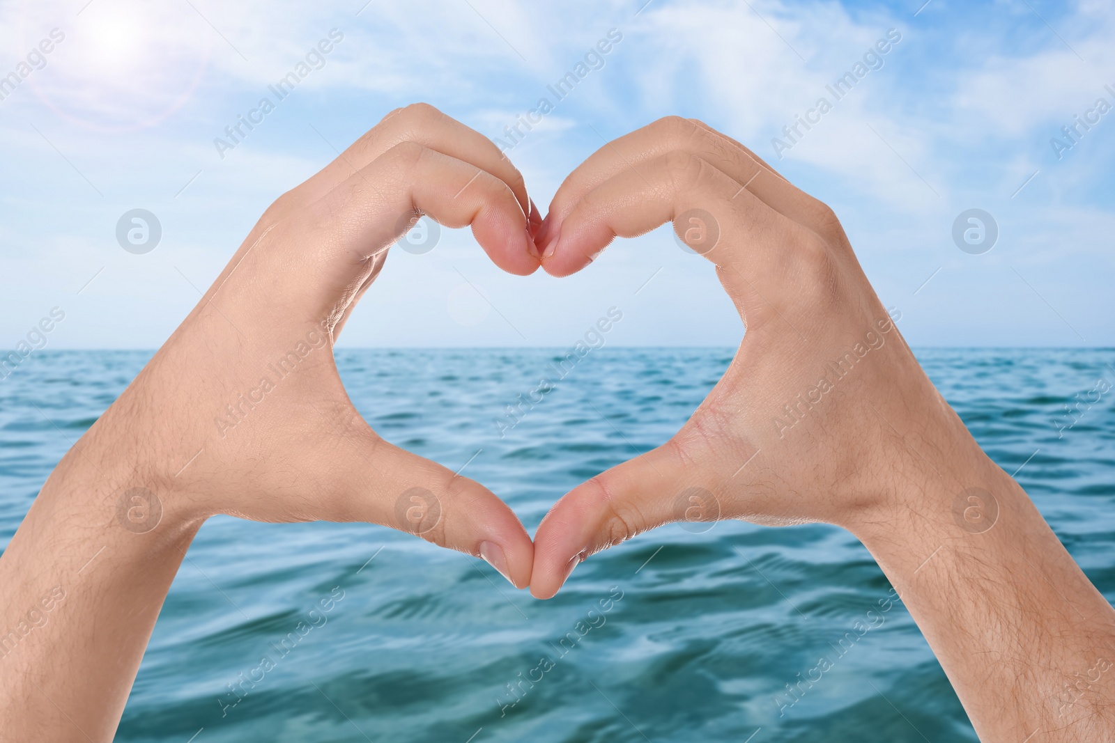 Image of Man making heart with hands near sea on sunny day, closeup