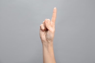 Photo of Woman showing number one on grey background, closeup. Sign language