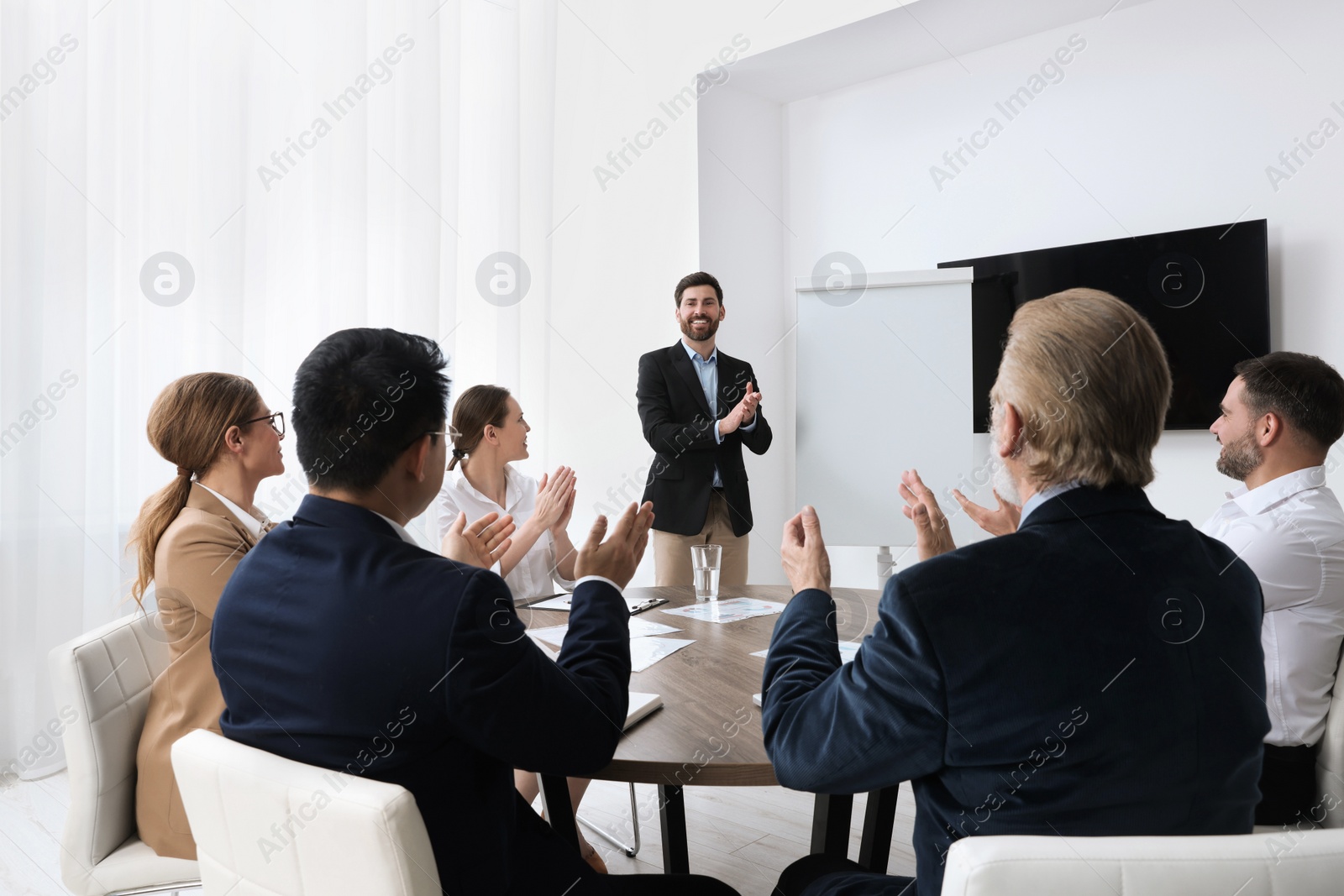 Photo of Business conference. Group of people listening to speaker report near tv screen in meeting room