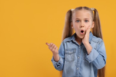 Photo of Special promotion. Emotional little girl pointing at something on orange background. Space for text