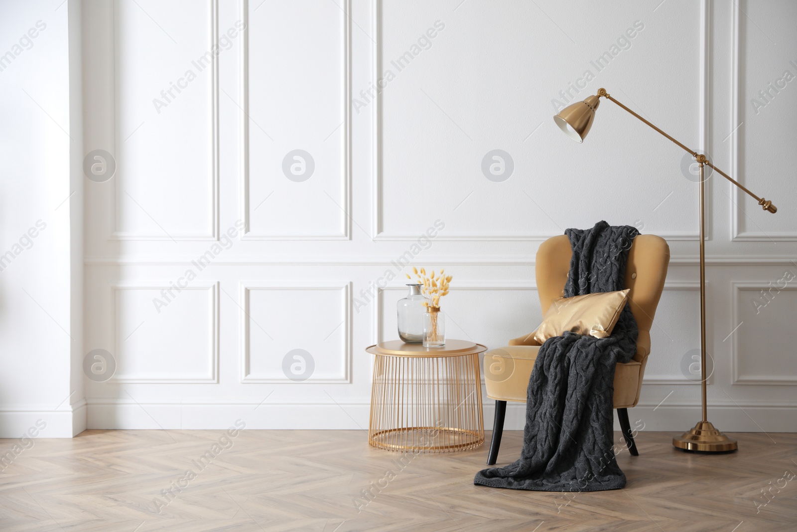 Photo of Modern armchair with soft blanket, coffee table and lamp in stylish room interior. Space for text