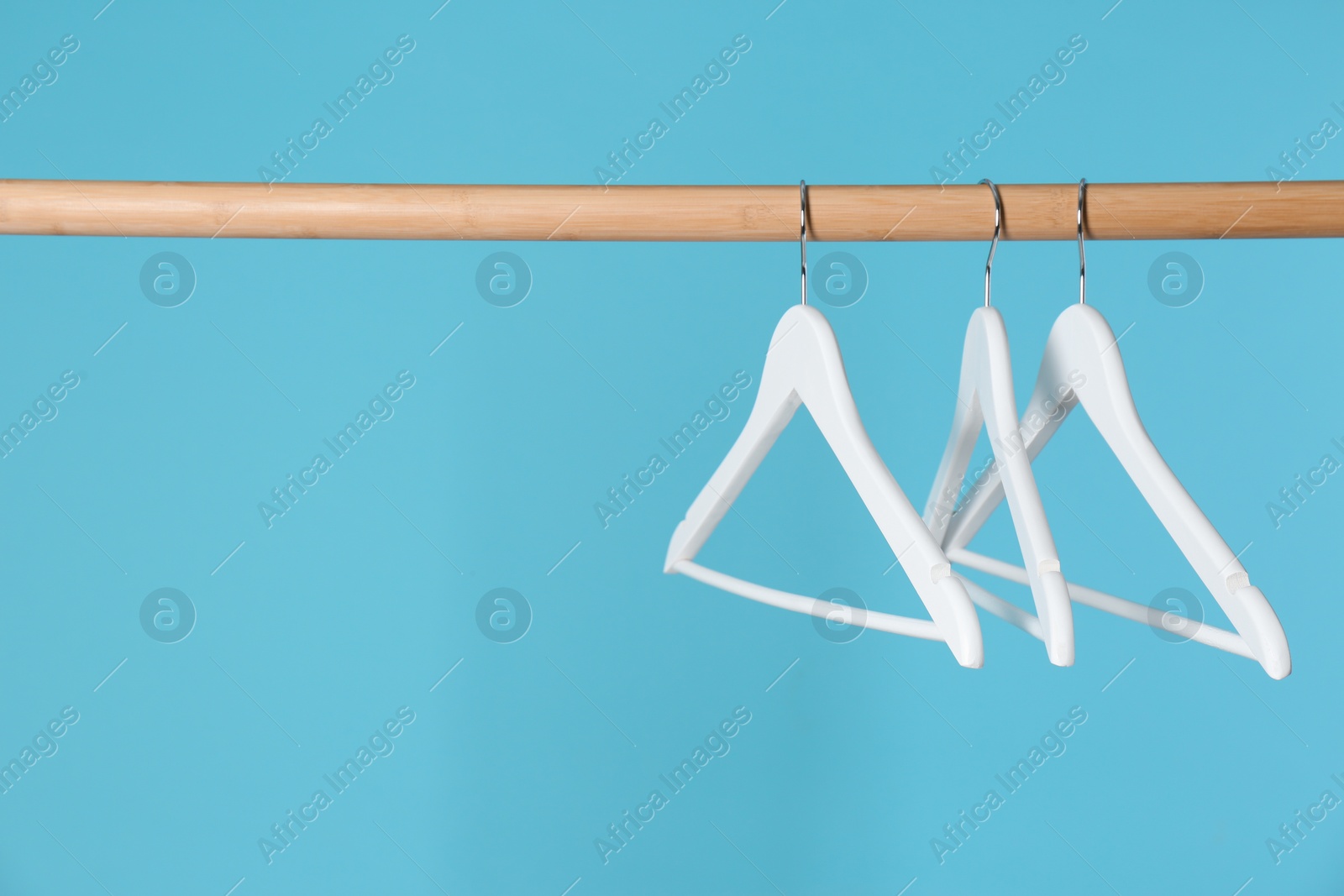 Photo of Wooden rack with clothes hangers on color background, space for text