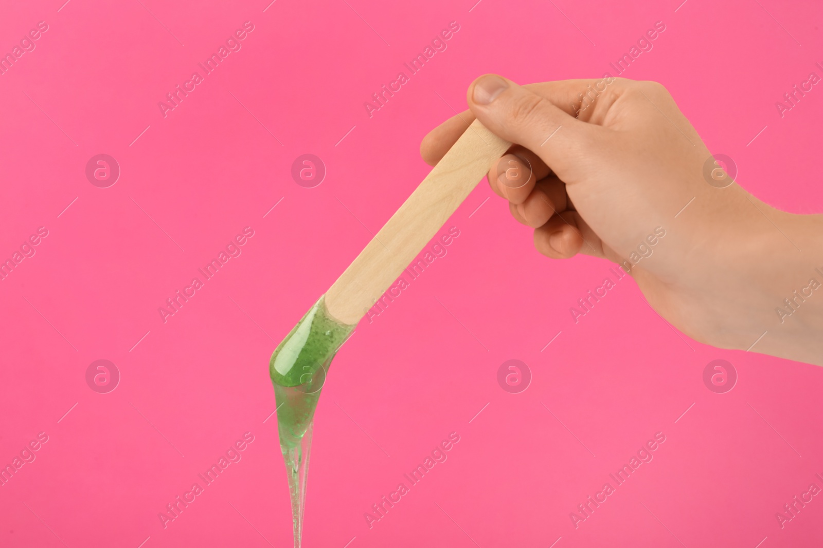 Photo of Woman holding spatula with hot depilatory wax on pink background, closeup