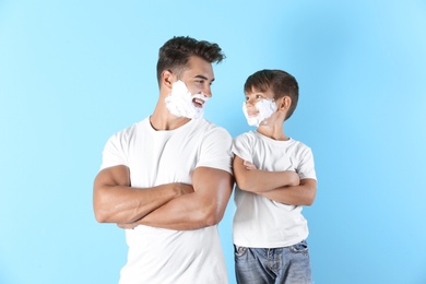 Photo of Father and son with shaving foam on faces against color background