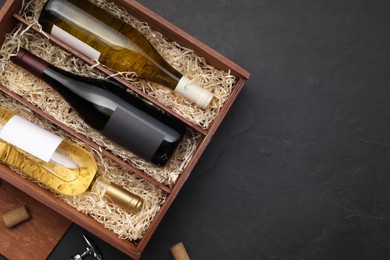 Photo of Box with wine bottles on dark textured table, top view. Space for text