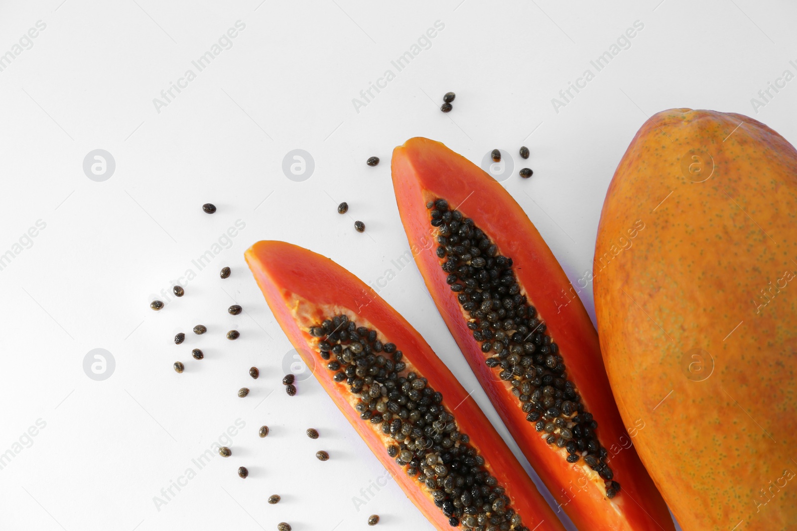 Photo of Fresh ripe cut and whole papaya fruits near scattered seeds on white background, flat lay. Space for text