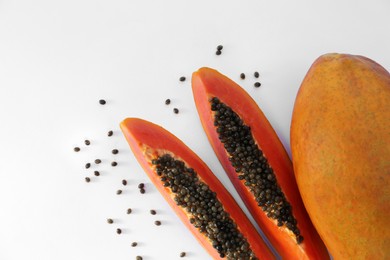 Photo of Fresh ripe cut and whole papaya fruits near scattered seeds on white background, flat lay. Space for text