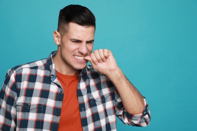 Man biting his nails on light blue background, space for text. Bad habit