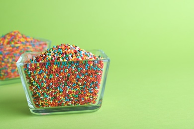 Photo of Colorful sprinkles in bowl on green background, space for text. Confectionery decor
