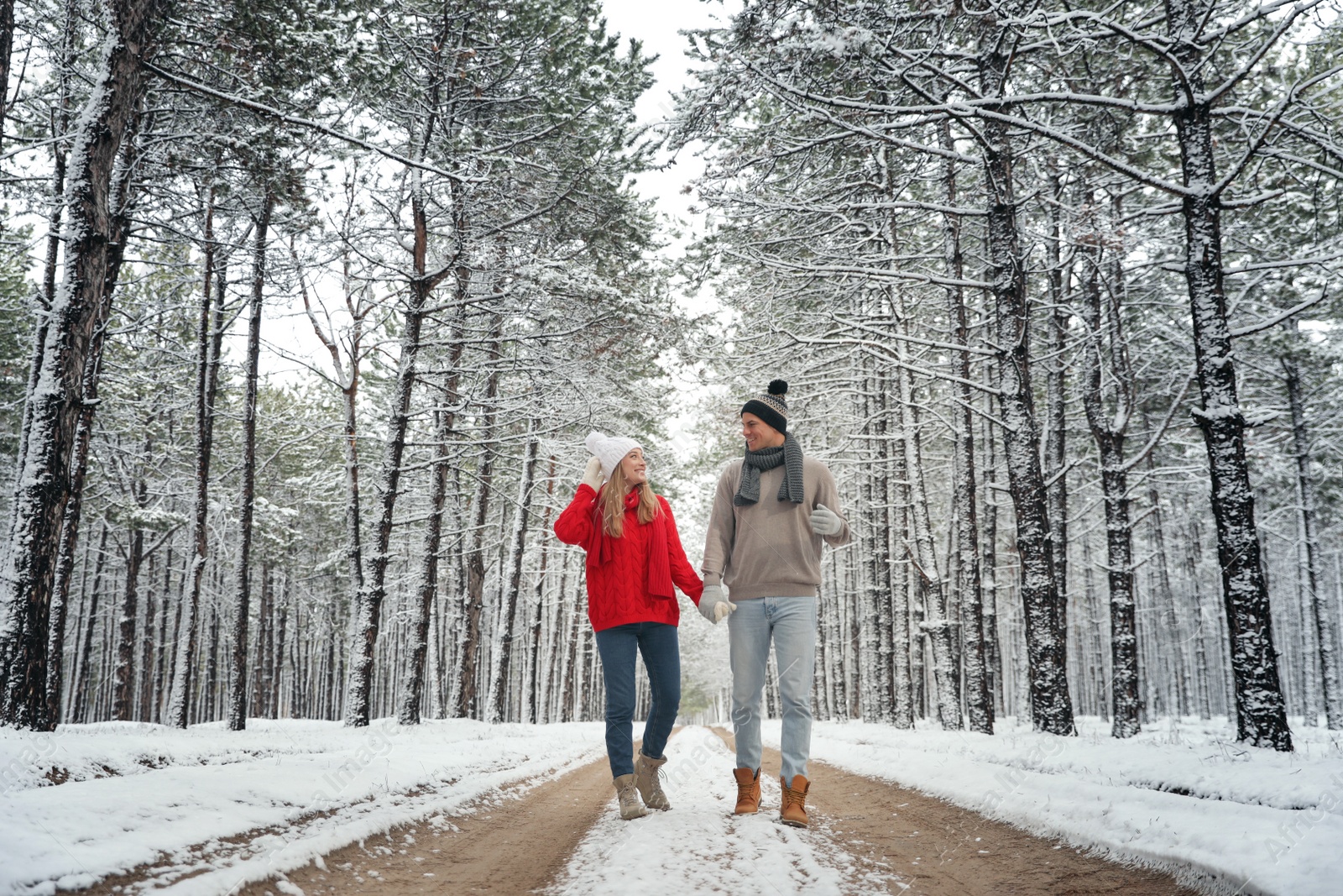 Photo of Beautiful happy couple walking through snowy forest on winter day