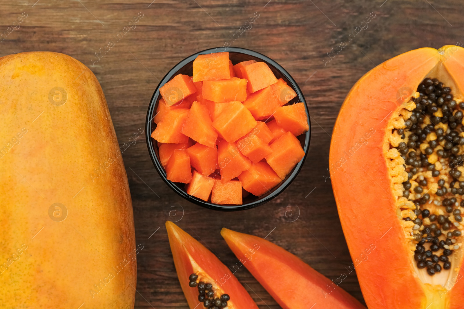 Photo of Tasty whole and cut papaya fruits on wooden table, flat lay