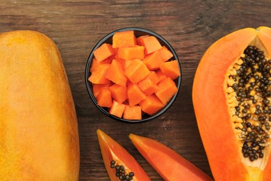 Photo of Tasty whole and cut papaya fruits on wooden table, flat lay