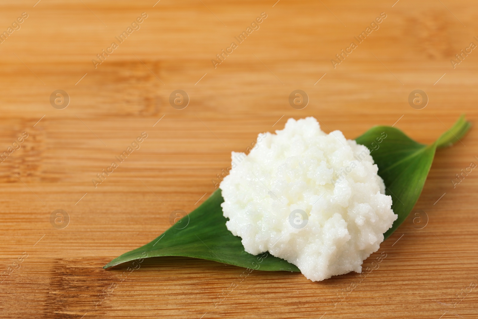 Photo of Shea butter with leaf on wooden background, top view. Space for text