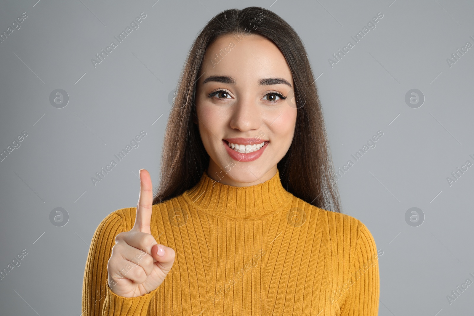 Photo of Woman in yellow turtleneck sweater showing number one with her hand on grey background