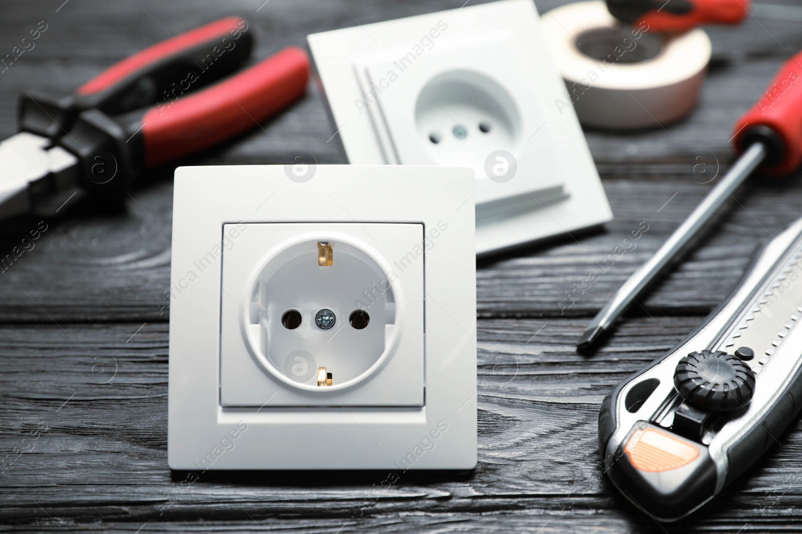 Photo of Power sockets and electrician's tools on black wooden table, closeup