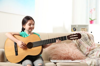 Photo of Cute little girl playing guitar on sofa in room. Space for text