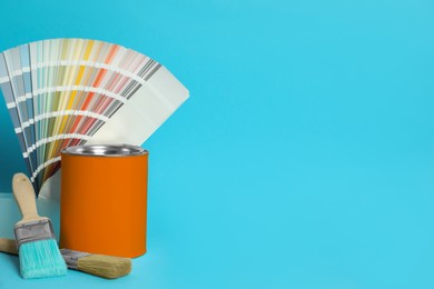 Photo of Can of orange paint, color palette samples and brushes on turquoise background. Space for text