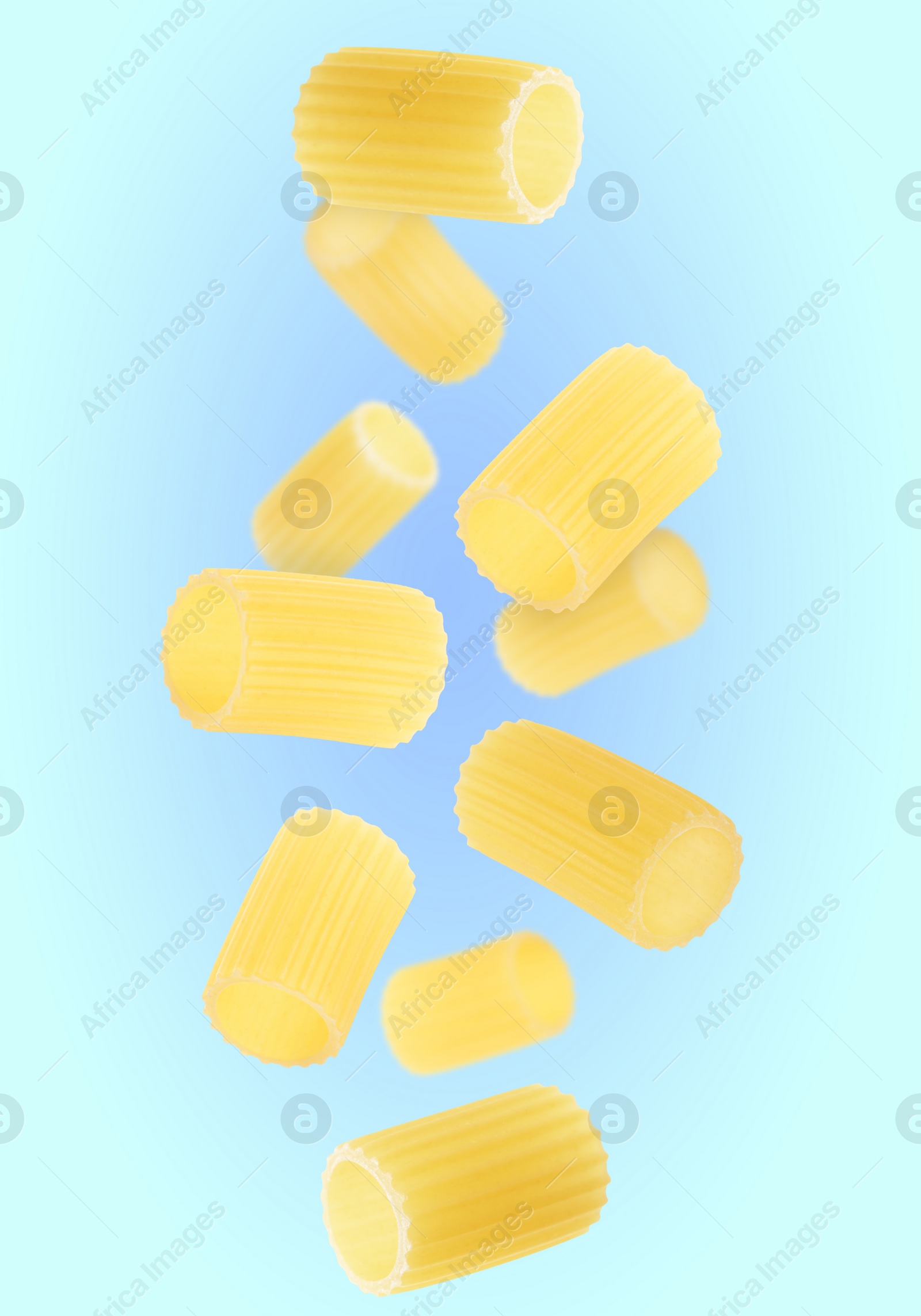 Image of Raw rigatoni pasta falling on light blue background