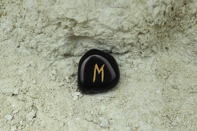 Black rune Ehwaz on stone outdoors, closeup