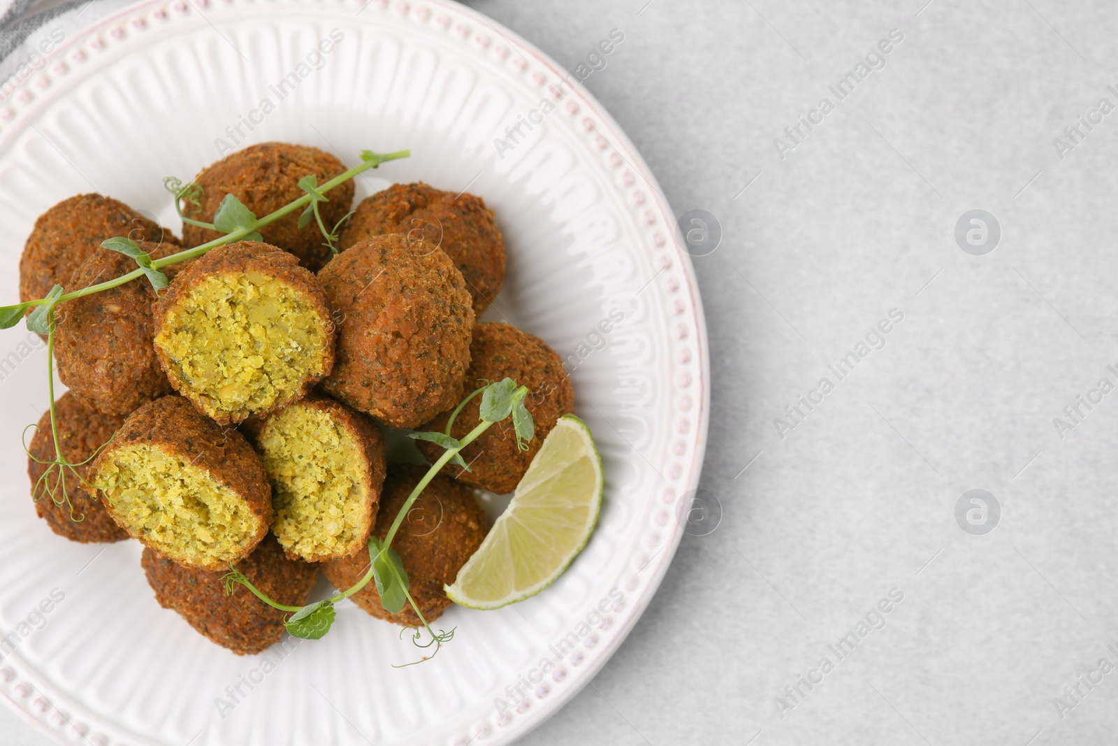 Photo of Delicious falafel balls, lime slice and microgreens on light table, top view. Space for text