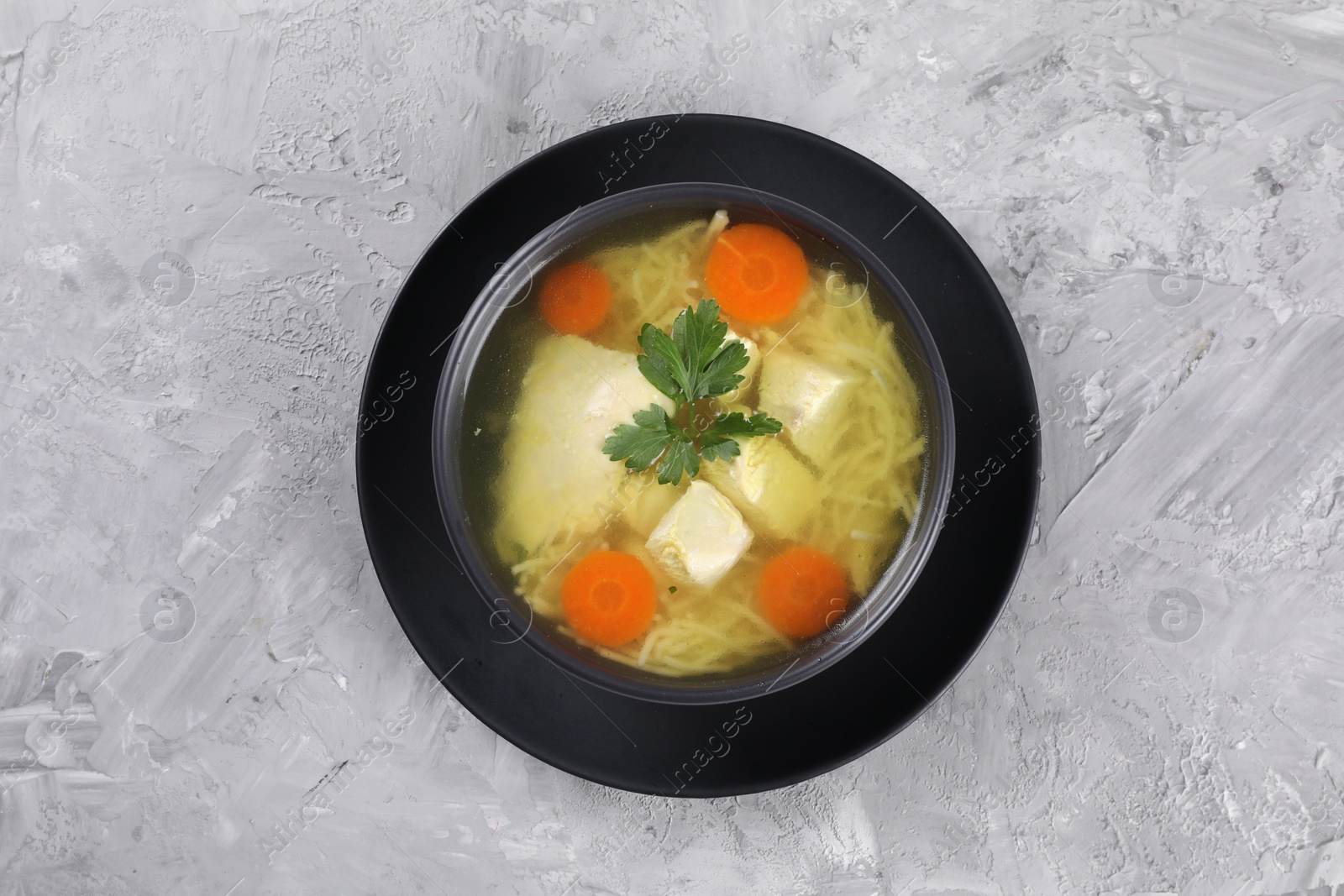 Photo of Tasty chicken soup with noodles, carrot and parsley in bowl on light textured table, top view