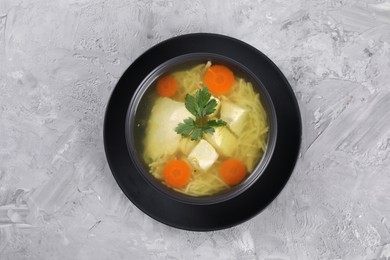 Tasty chicken soup with noodles, carrot and parsley in bowl on light textured table, top view