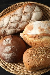 Wicker basket with different types of fresh bread on black table, top view