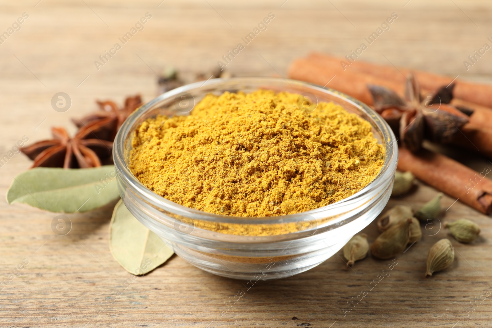 Photo of Curry powder in bowl and other spices on wooden table, closeup