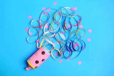 Photo of Beautiful serpentine and confetti bursting out of party popper on light blue background, flat lay
