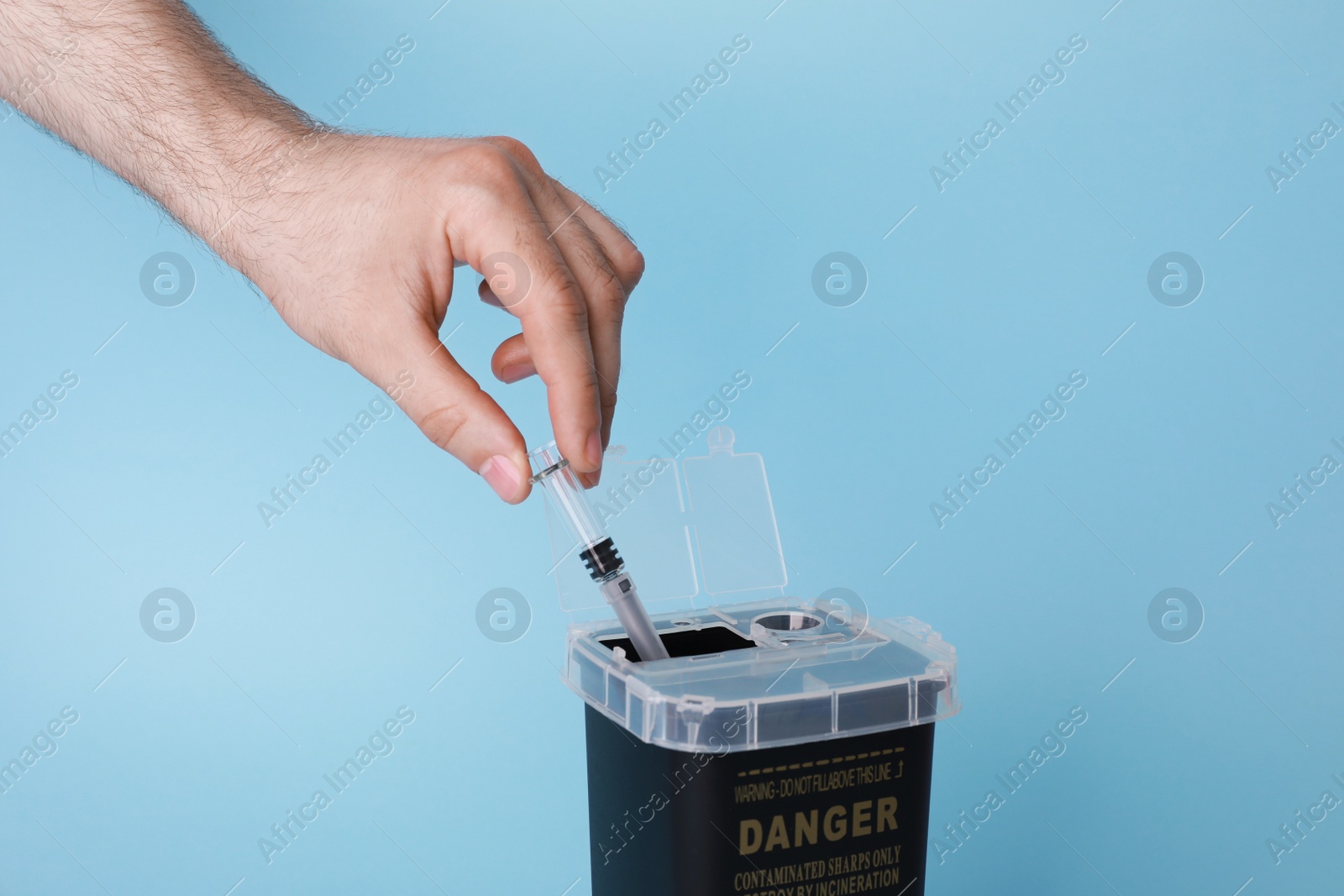 Photo of Man throwing used syringe into sharps container on light blue background, closeup