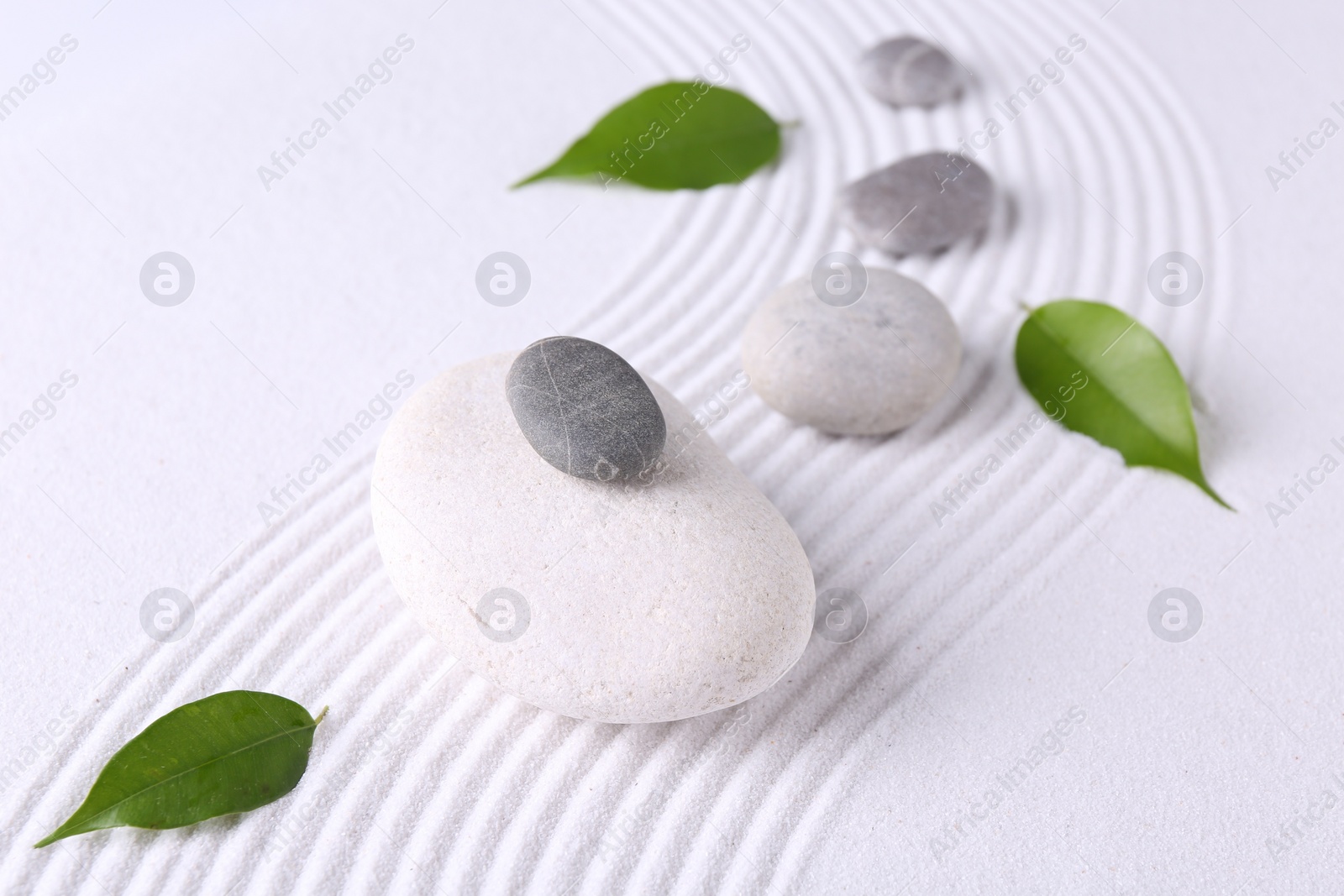 Photo of Zen garden stones and green leaves on white sand with pattern