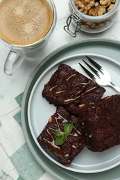 Photo of Delicious chocolate brownies with nuts, caramel sauce and coffee on white marble table, flat lay