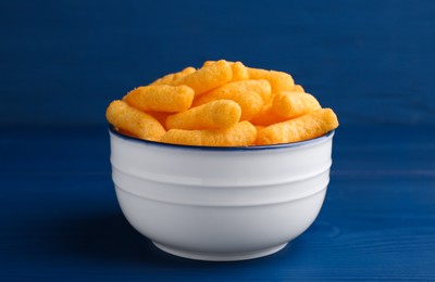 Photo of Bowl of tasty cheesy corn puffs on blue wooden table