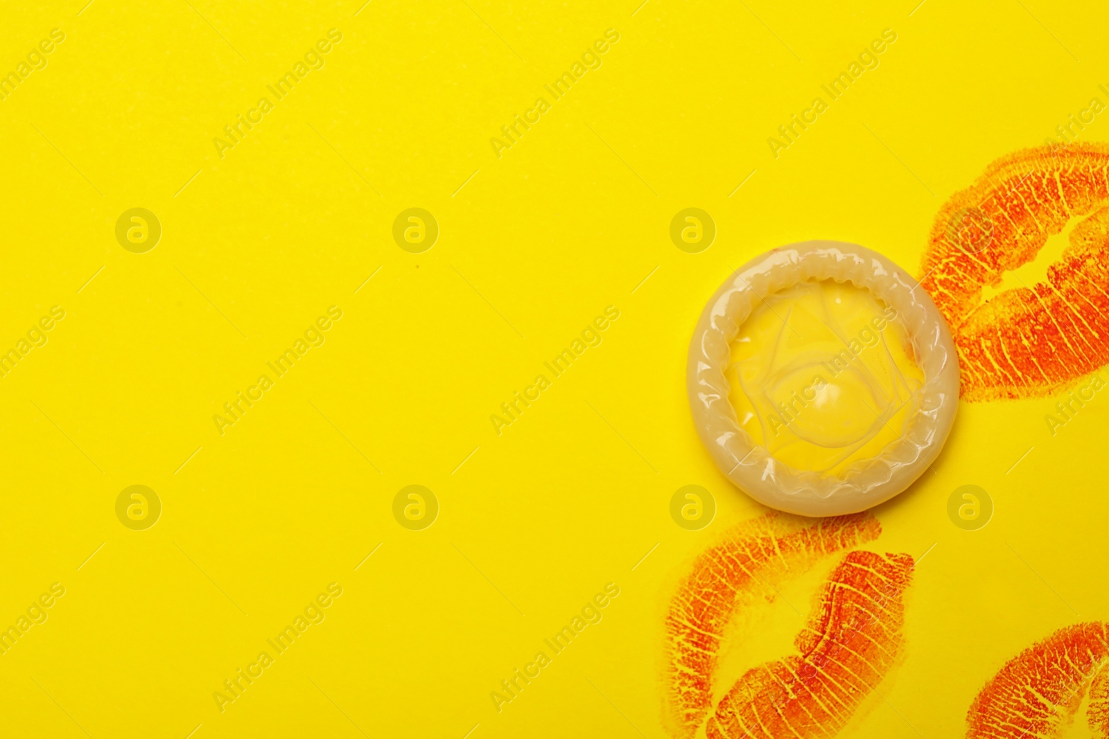 Photo of Condom with lipstick kiss marks and space for text on yellow background, top view. Safe sex