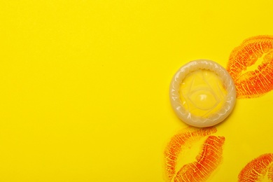 Condom with lipstick kiss marks and space for text on yellow background, top view. Safe sex