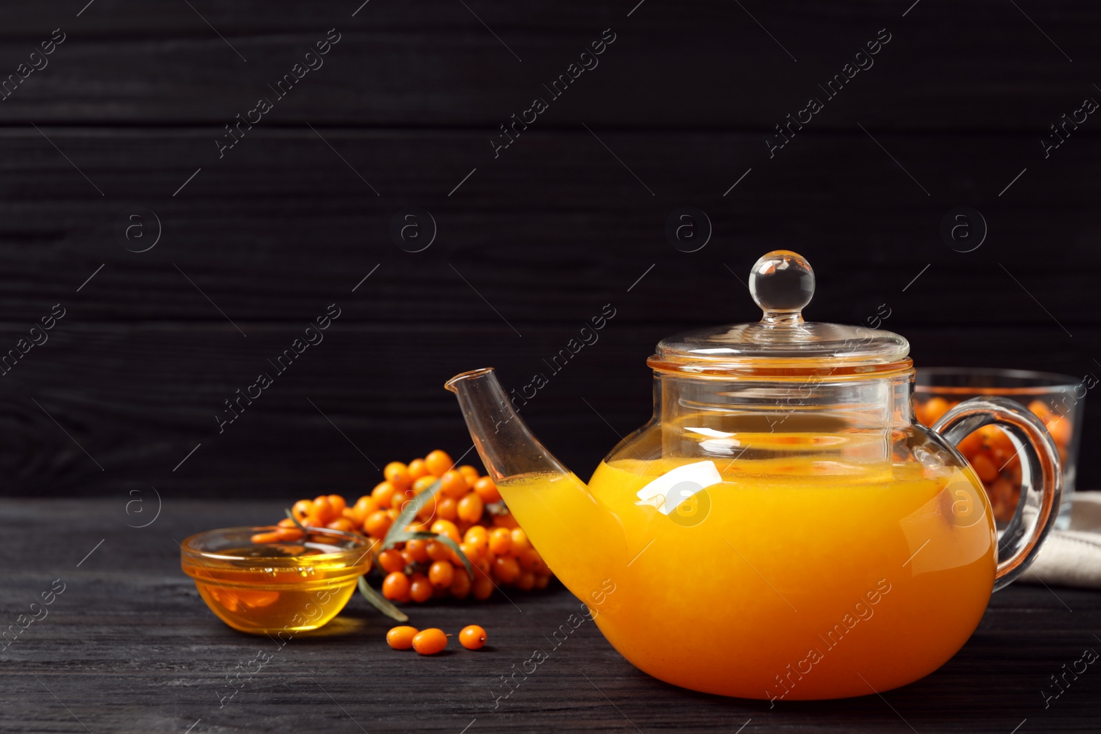 Photo of Delicious sea buckthorn tea and fresh berries on black wooden table. Space for text