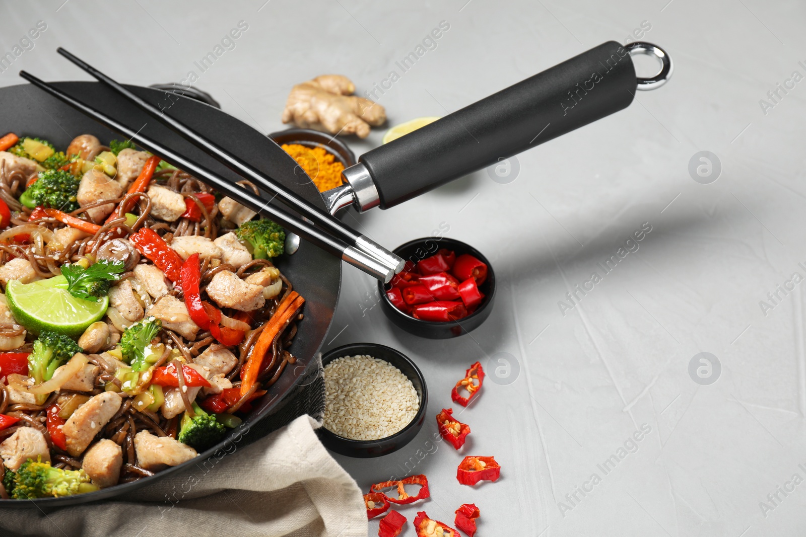 Photo of Stir-fry. Tasty noodles with meat in wok, chopsticks and ingredients on grey textured table