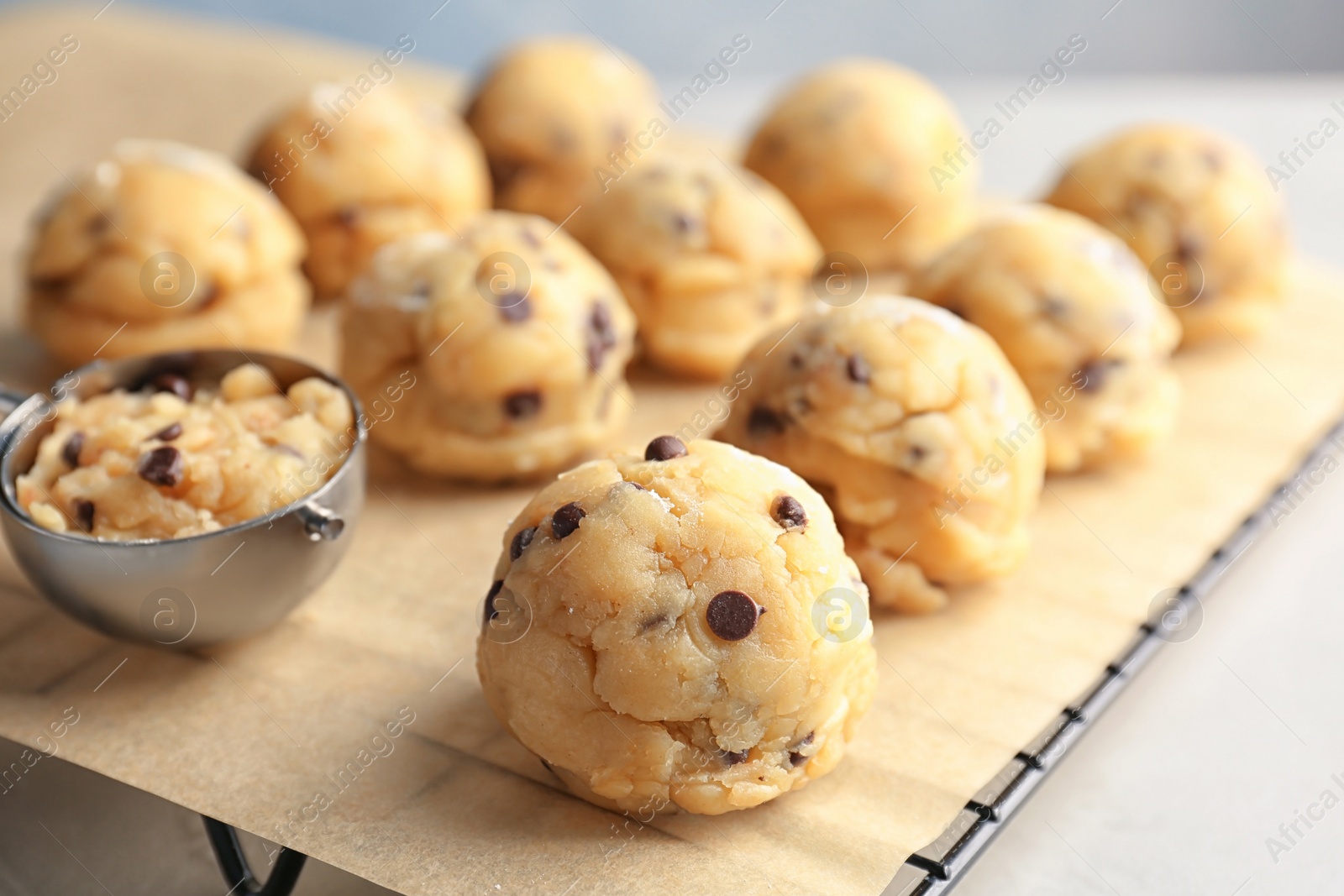 Photo of Raw cookie dough with chocolate chips and scoop on parchment paper, closeup