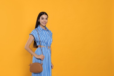 Photo of Beautiful young woman with stylish bag on orange background, space for text