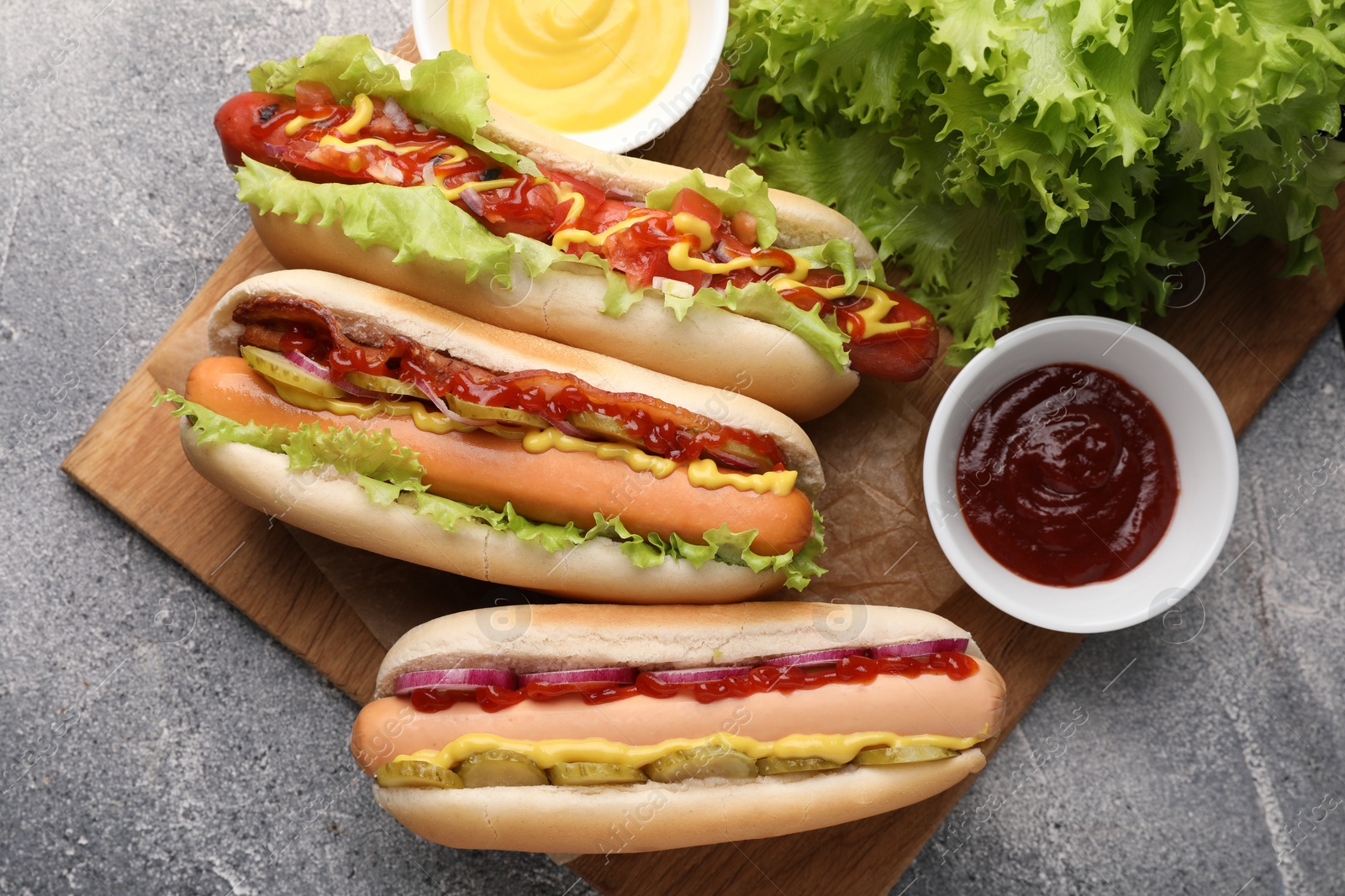 Photo of Delicious hot dogs with different toppings served on grey table, flat lay