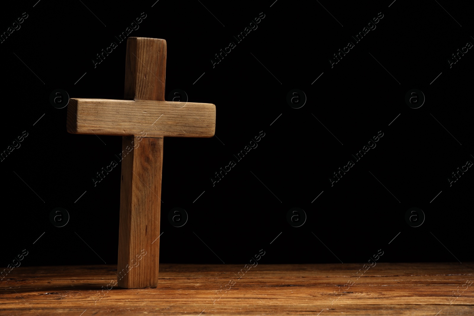 Photo of Cross on wooden table against black background, space for text. Religion of Christianity