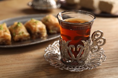 Photo of Glass of traditional Turkish tea in vintage holder and fresh baklava on wooden table, closeup