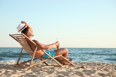 Photo of Young man relaxing in deck chair on beach near sea