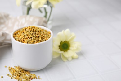 Photo of Fresh bee pollen granules and flower on white tiled table, closeup. Space for text