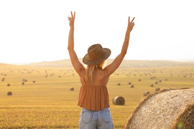 Photo of Hippie woman showing peace signs in field, back view