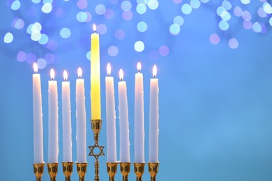 Photo of Hanukkah celebration. Menorah with burning candles on light blue background with blurred lights, space for text