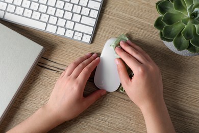 Photo of Woman wiping wireless mouse with paper towel at wooden table, closeup
