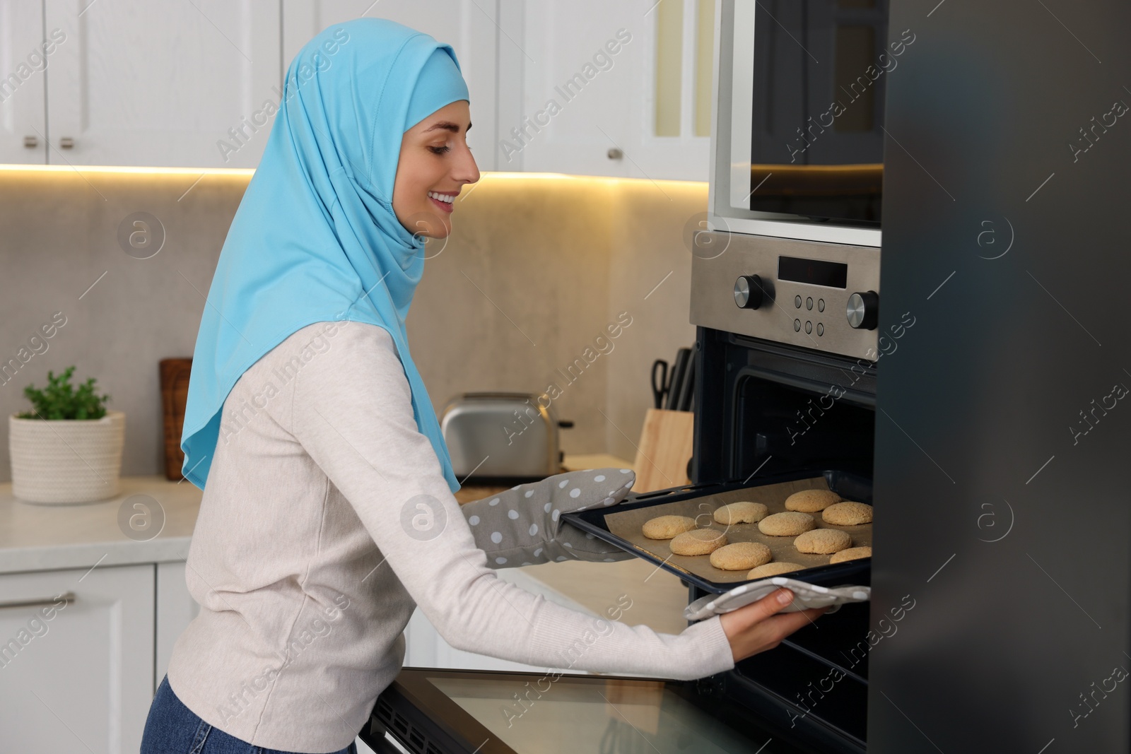 Photo of Muslim woman baking delicious cookies in oven at home